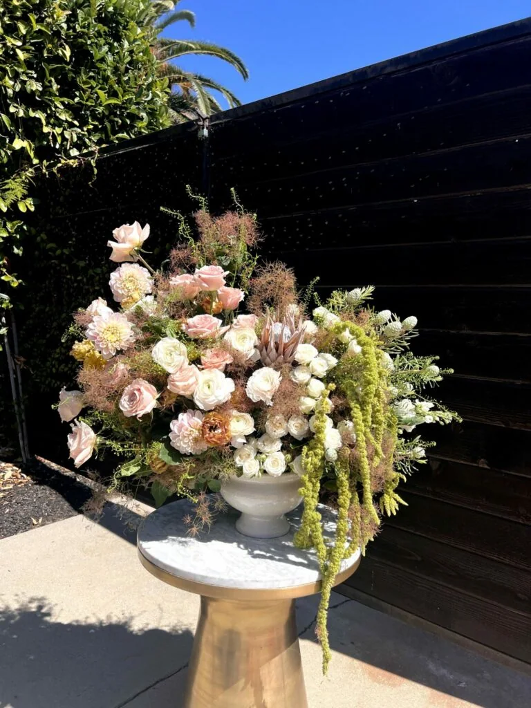 Sculptural blush floral arrangement with cascading green amaranthus on a gold pedestal